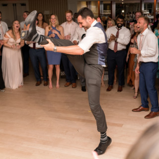 Groom dancing energetically at Beauport wedding reception surrounded by cheering guests in Gloucester, Massachusetts.