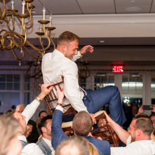 Groom lifted on chair by friends during joyful wedding celebration in elegant Gloucester ballroom.