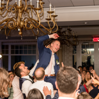 Groom lifted and cheered during joyful wedding reception in Gloucester, Massachusetts.