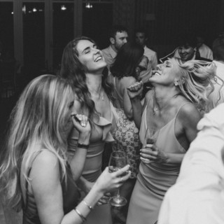 Black and white photo of joyful women dancing and laughing at an elegant wedding celebration.