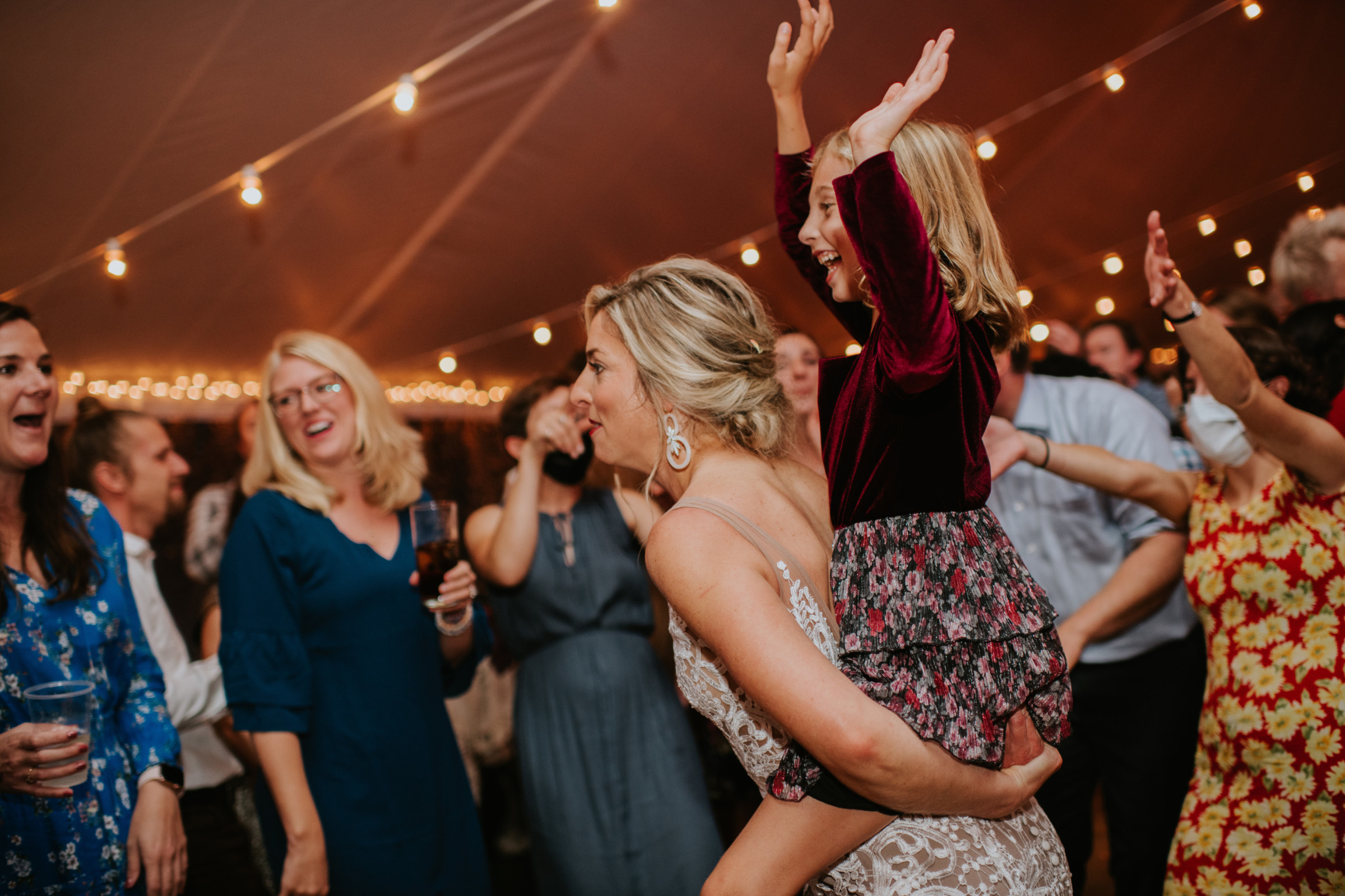 Bride carrying joyful child during lively wedding celebration at Toad Hill Farm in Franconia, New Hampshire.