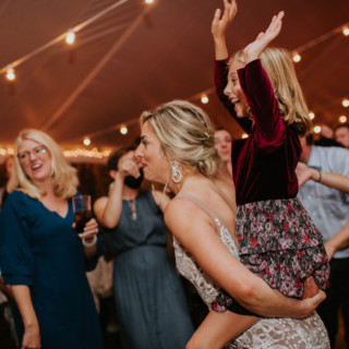 Bride carrying joyful child during lively wedding celebration at Toad Hill Farm in Franconia, New Hampshire.