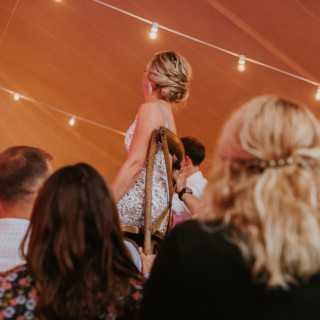 Bride lifted on chair during joyful tent wedding celebration at Toad Hill Farm, Franconia NH.