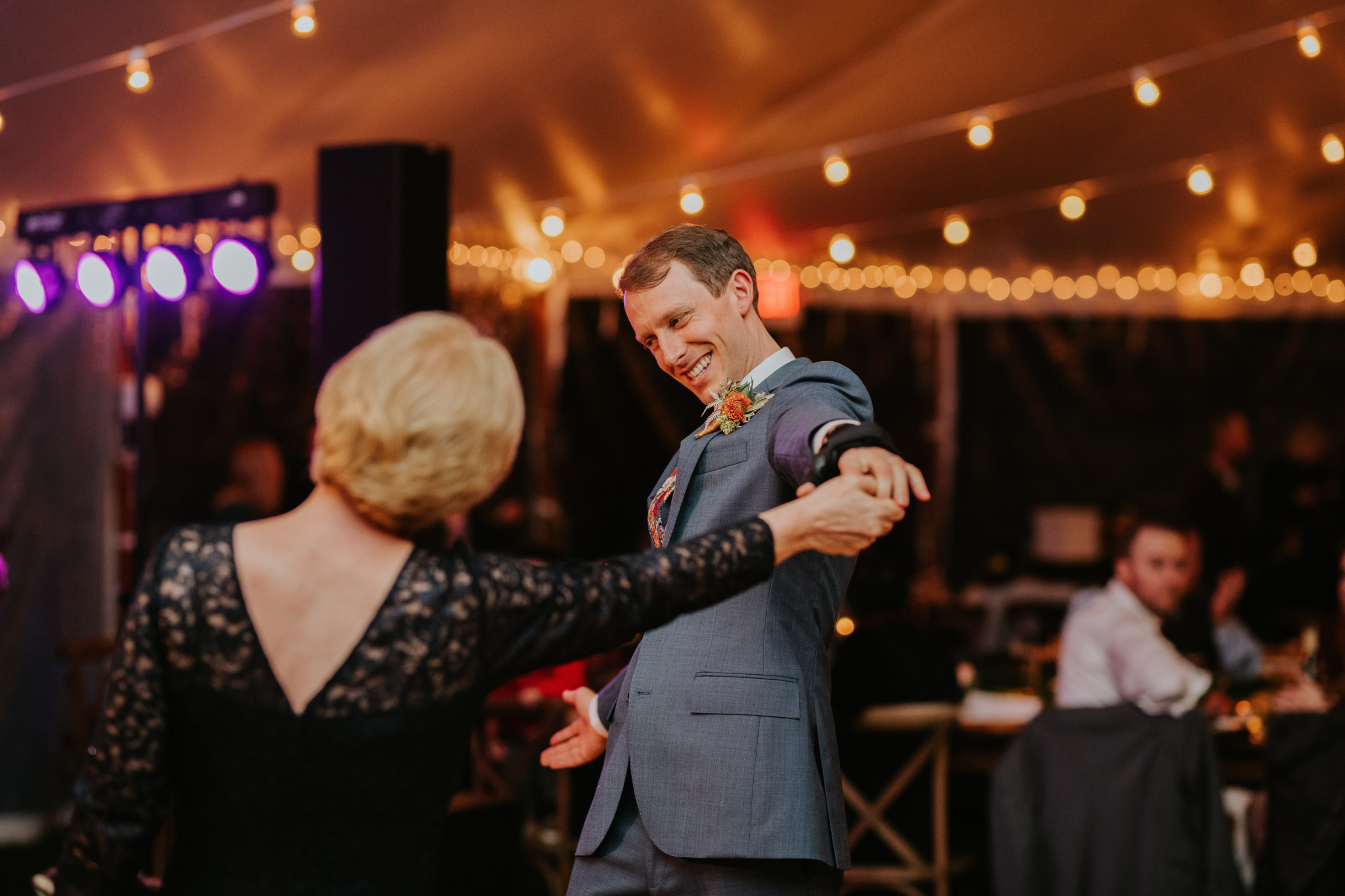 Groom dancing joyfully with his mother under string lights at Toad Hill Farm wedding.