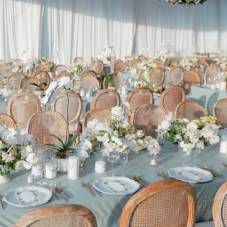 Elegant blue and white wedding reception setup with floral centerpieces and candlelit banquet tables in Bali.