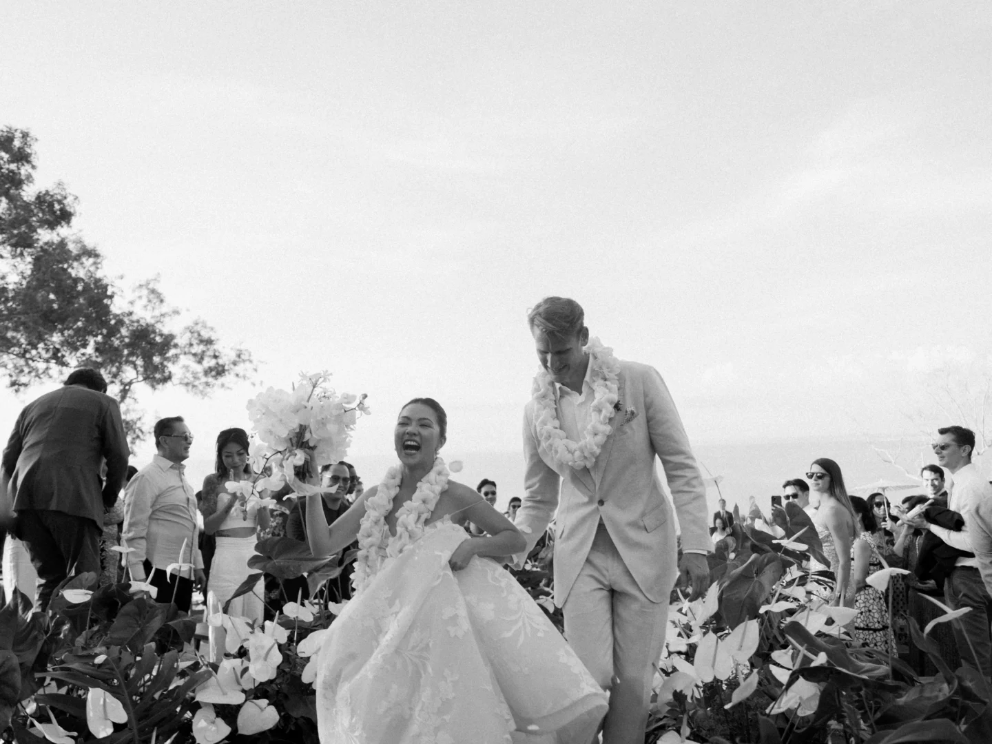 Bride and groom walking joyfully through tropical garden at Bali wedding celebration.