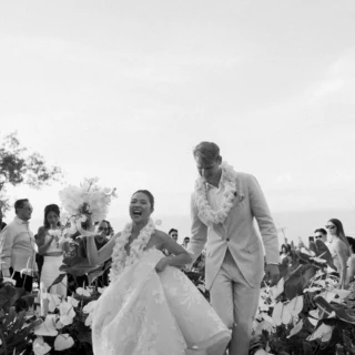 Bride and groom walking joyfully through tropical garden at Bali wedding celebration.