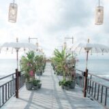 Serene seaside pier at Ayana Resort Bali with tropical plants, white umbrellas, and ocean views.
