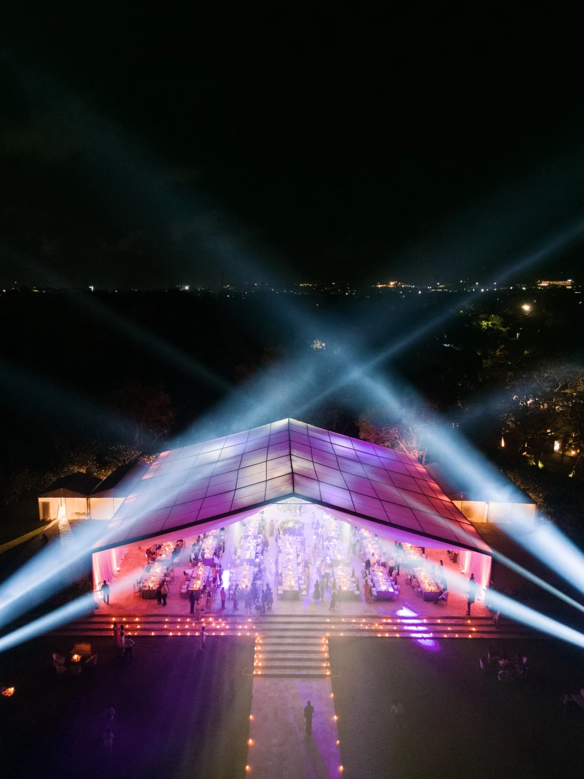 Aerial view of a vibrant nighttime wedding reception under a glowing transparent tent in Bali.