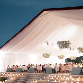 Romantic outdoor wedding reception under draped marquee tent with candlelit steps and elegant dinner setting.