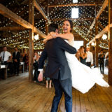 Bride and groom dancing joyfully under warm fairy lights at rustic Cunningham Farm wedding.