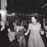 Guests dancing joyfully at a rustic barn wedding reception in Maine.