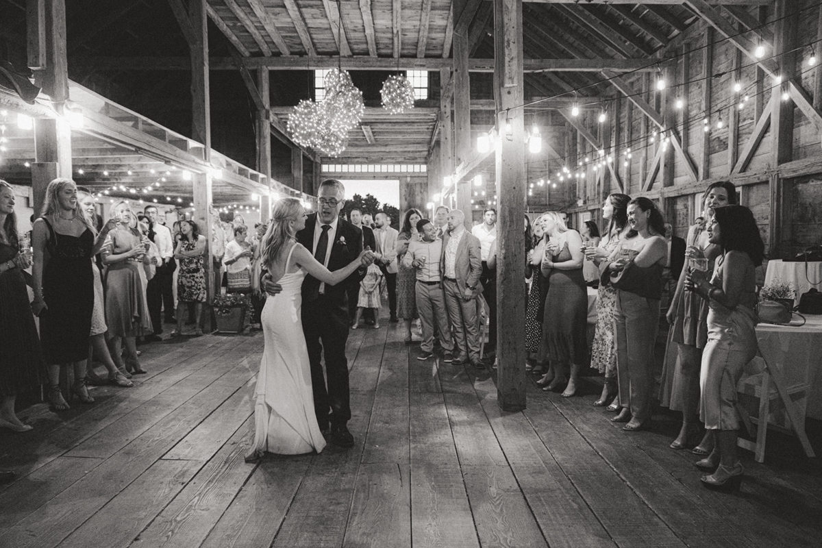 Bride and groom share first dance under string lights in rustic barn wedding celebration.