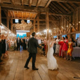 Bride and groom share first dance under string lights in rustic barn wedding at Shady Lane Farm.