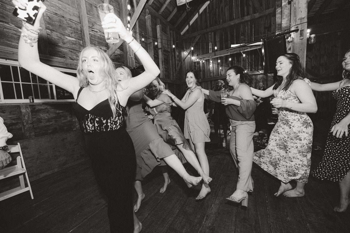 Women dancing joyfully at rustic barn wedding reception in New Gloucester, Maine.