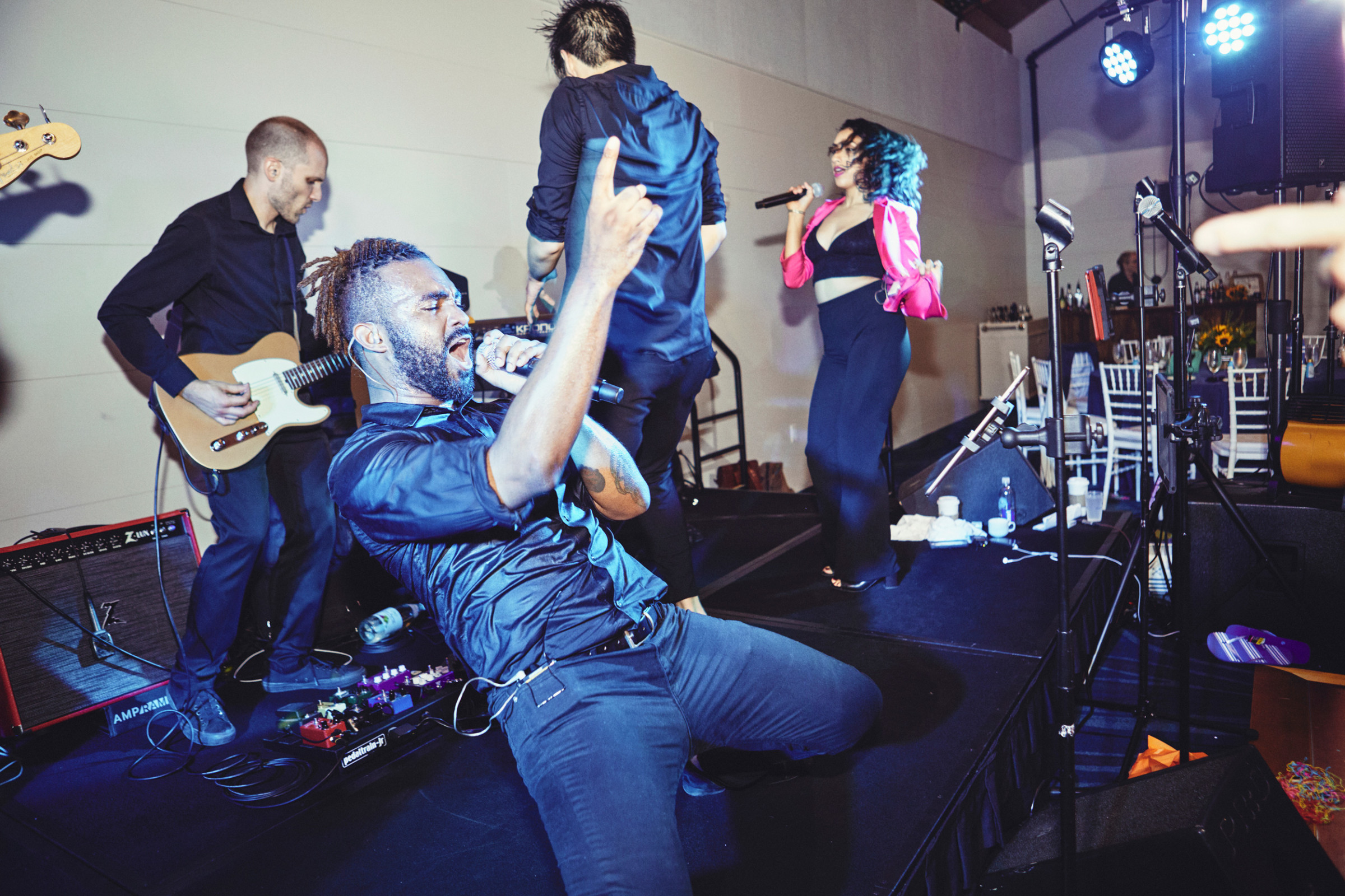 Energetic live band performing indoors with passionate singers and guitarist under vibrant stage lighting.