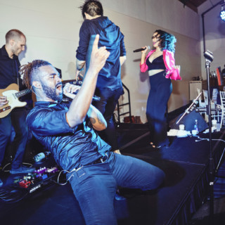 Energetic live band performing indoors with passionate singers and guitarist under vibrant stage lighting.