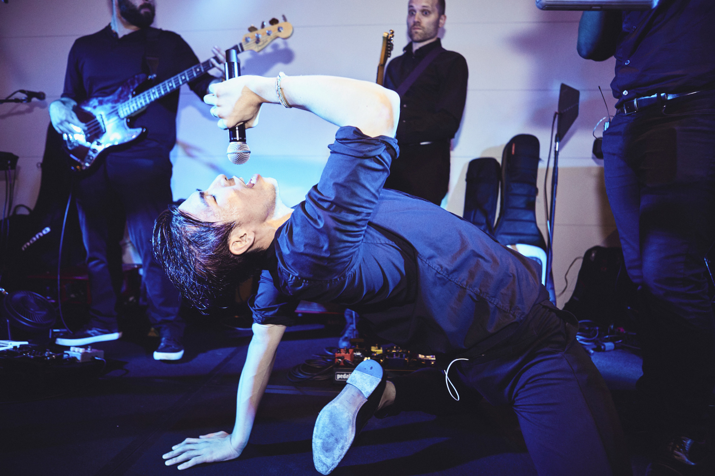 Rock singer performing passionately on stage with band under dramatic blue and violet concert lighting.