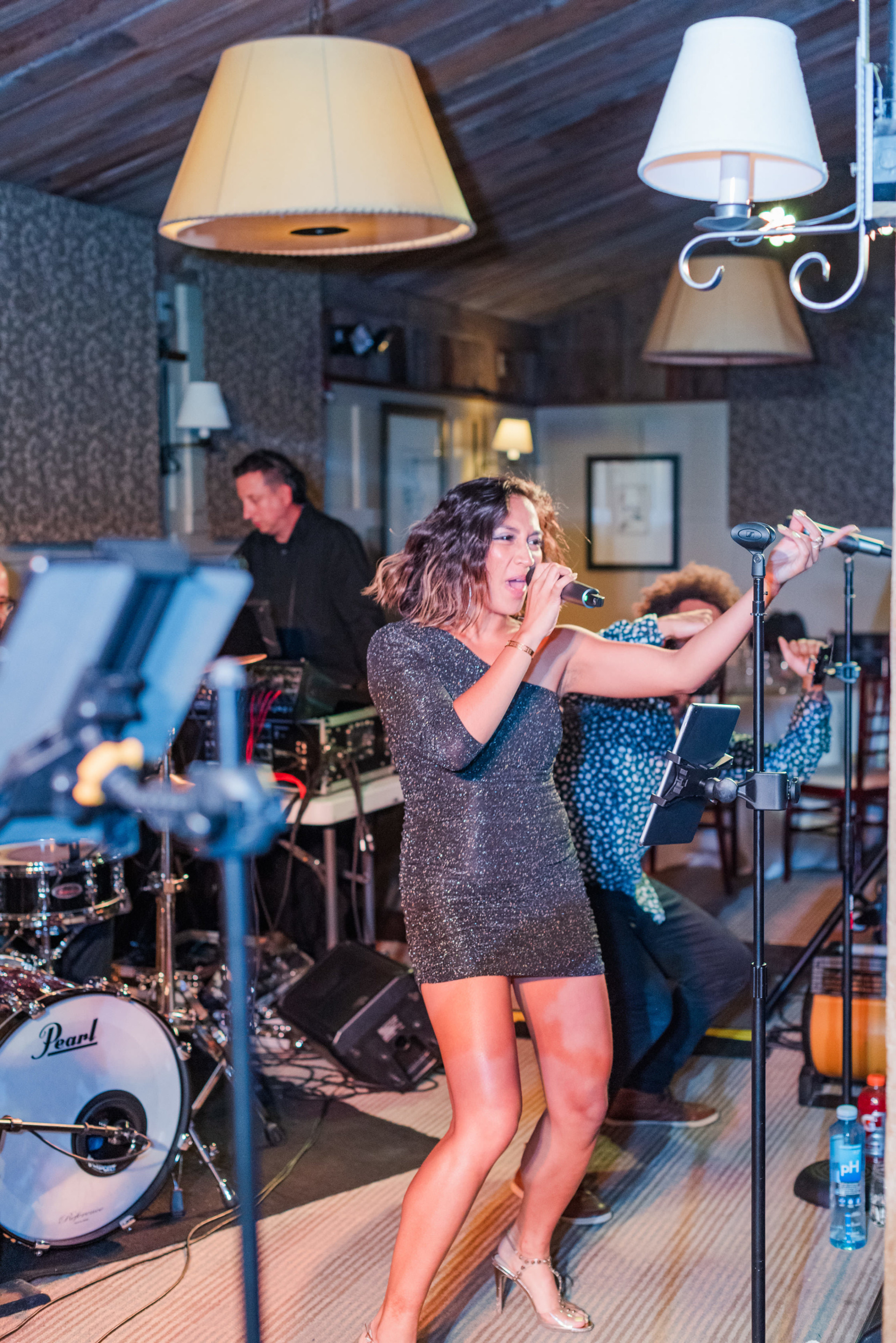 Female singer in silver dress performing live with band in warm, intimate indoor venue.