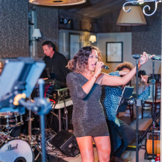 Female singer in silver dress performing live with band in warm, intimate indoor venue.