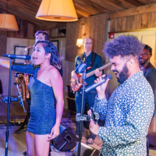 Energetic live band performing indoors with passionate singers and warm, colorful stage lighting.