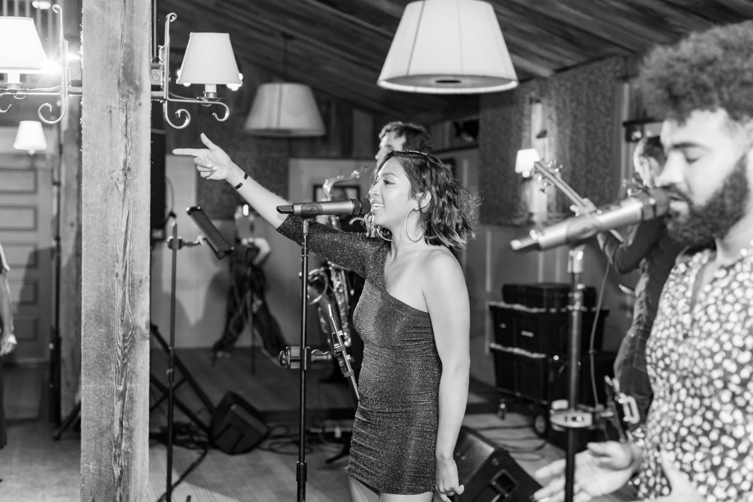 Black-and-white photo of lively female singer performing with band at rustic indoor wedding venue.
