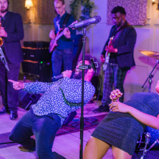 Energetic live band performance with passionate singers and musicians in a colorful indoor venue.