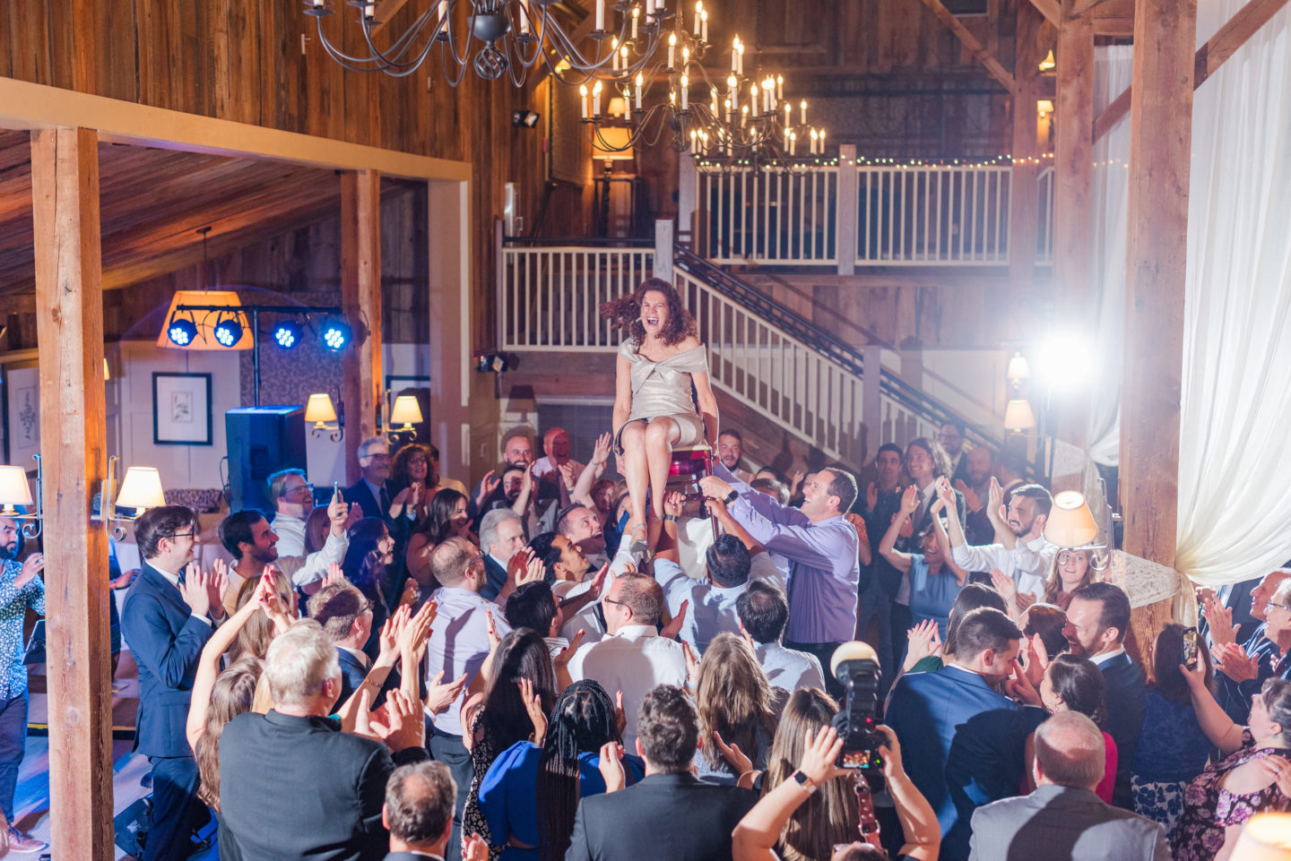 Bride lifted on a chair during joyful rustic wedding celebration at Gibbet Hill, Groton MA.