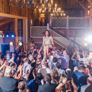 Bride lifted on a chair during joyful rustic wedding celebration at Gibbet Hill, Groton MA.