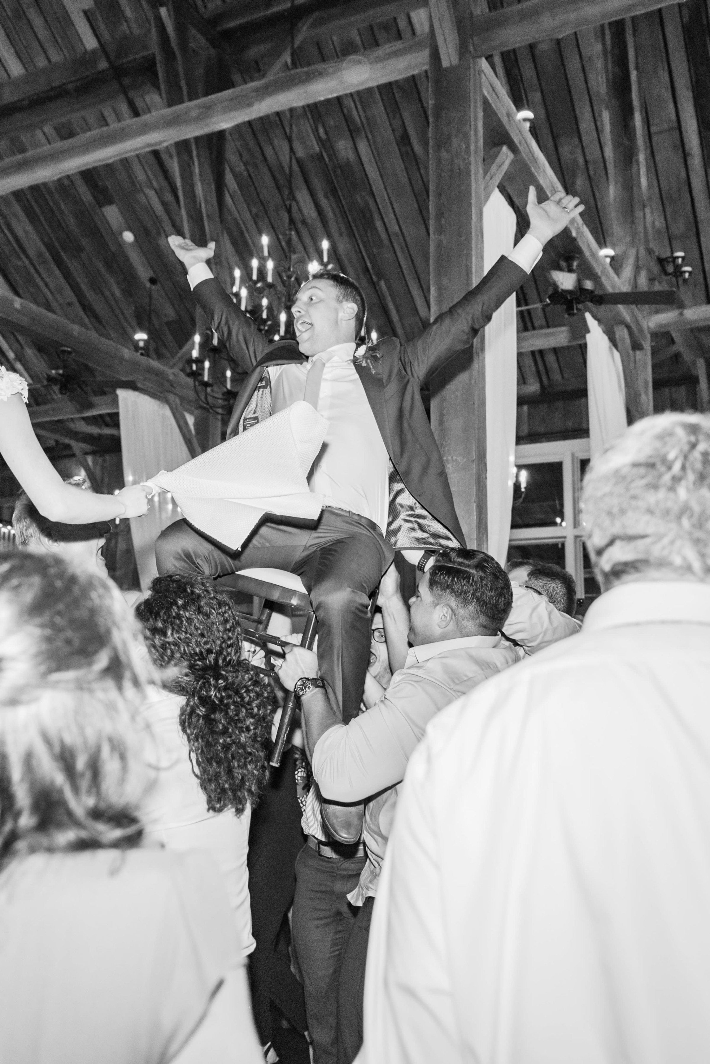 Groom lifted on chair during joyful wedding celebration at Gibbet Hill in Groton, Massachusetts.