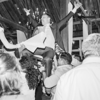 Groom lifted on chair during joyful wedding celebration at Gibbet Hill in Groton, Massachusetts.