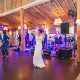 Bride and groom dancing joyfully at rustic barn wedding with live band in warm lighting.