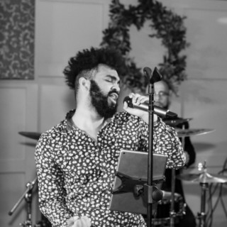 Emotional black and white photo of soulful male singer performing live with drummer in background.