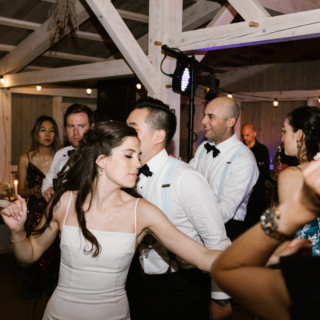 Bride dancing with guests under warm string lights at rustic Marianmade Farm wedding in Wiscasset Maine.