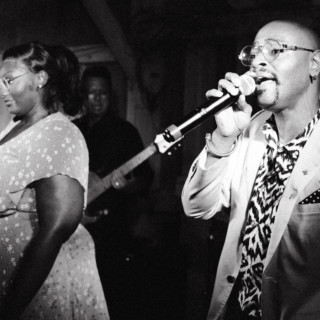 Black-and-white photo of a soulful live music performance with singers and band on stage.