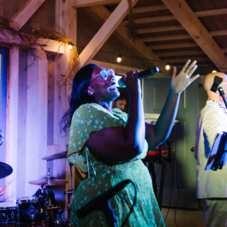 Singer in green floral dress performing with live band at rustic barn wedding in Maine.