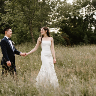 Bride and groom holding hands in a sunlit green field at Marianmade Farm wedding.