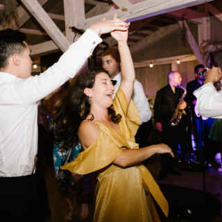 Couple dancing joyfully at rustic barn wedding with live band and string lights.