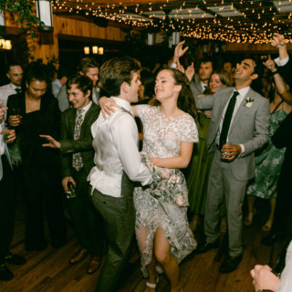 Couple dancing at joyful Migis Lodge wedding reception under warm string lights in South Casco, Maine.