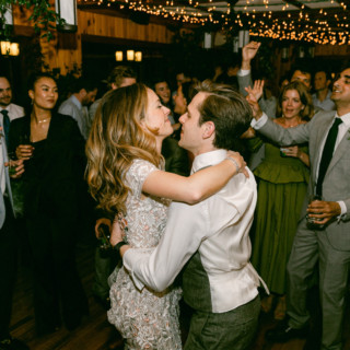 Bride and groom share joyful first dance at rustic wedding reception with cheering guests.