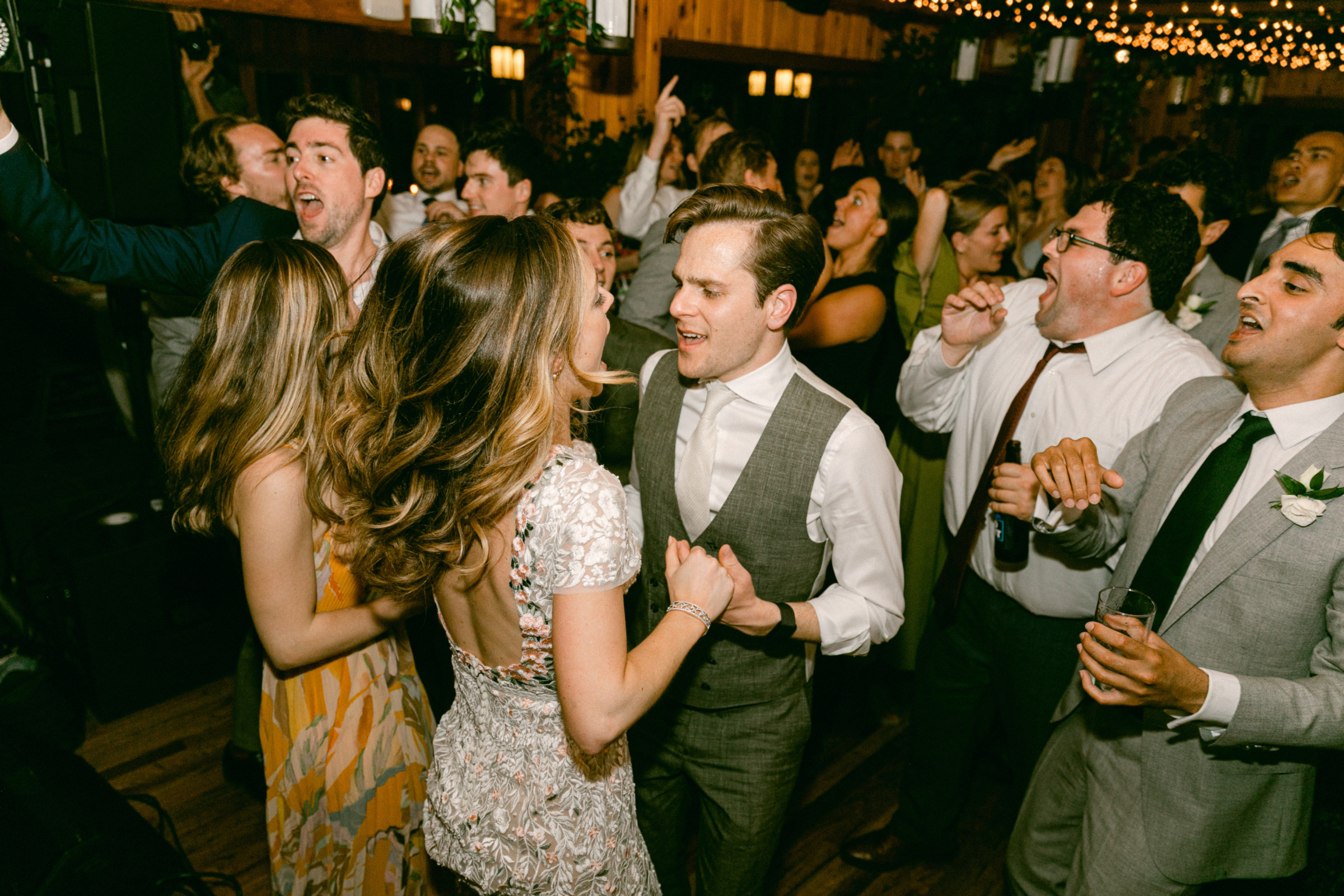 Bride and groom dancing joyfully among cheering guests at Migis Lodge wedding in Maine.