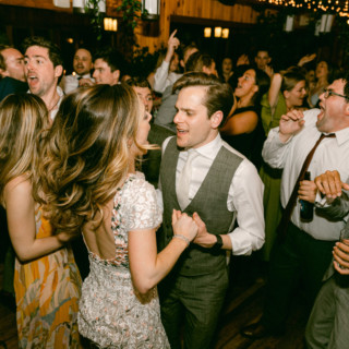 Bride and groom dancing joyfully among cheering guests at Migis Lodge wedding in Maine.