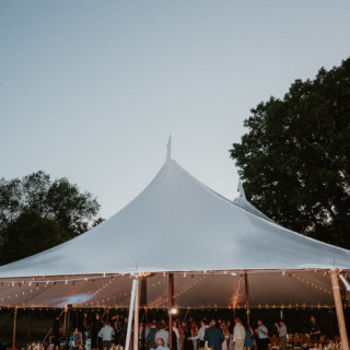 Elegant outdoor wedding reception at dusk under a glowing white tent in Vermont.
