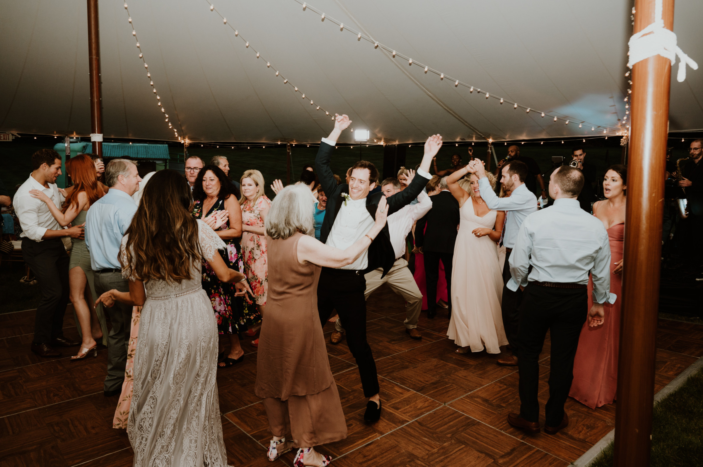 Guests dancing joyfully under glowing string lights at an elegant Vermont wedding reception.