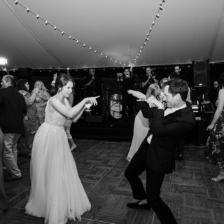 Bride and groom dancing joyfully under string lights at a lively Vermont wedding reception.