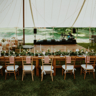 Elegant outdoor wedding reception under white tent with wooden tables, string lights, and floral décor.