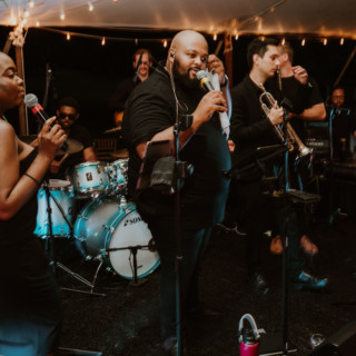 Energetic live wedding band performing under warm string lights at River Road Farm in Manchester, Vermont.