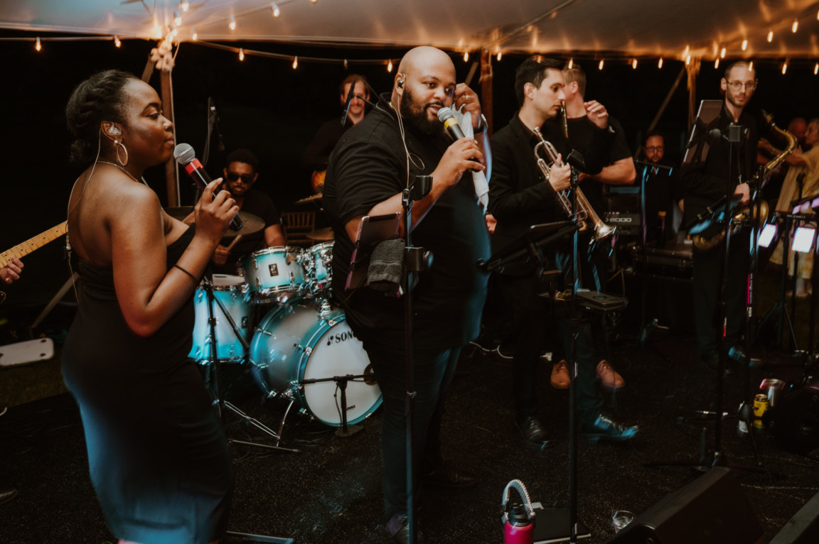 Energetic live wedding band performing under warm string lights at River Road Farm in Manchester, Vermont.