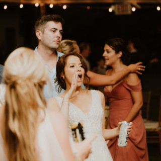 Bride cheering with guests under string lights at lively outdoor Vermont wedding reception.