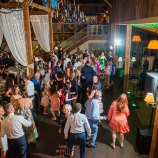Guests dancing and celebrating at a rustic barn wedding reception with live music and warm lighting.